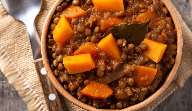 Ragout de estofado de lentejas con calabaza y zanahoria en un tazón sobre mesa de madera